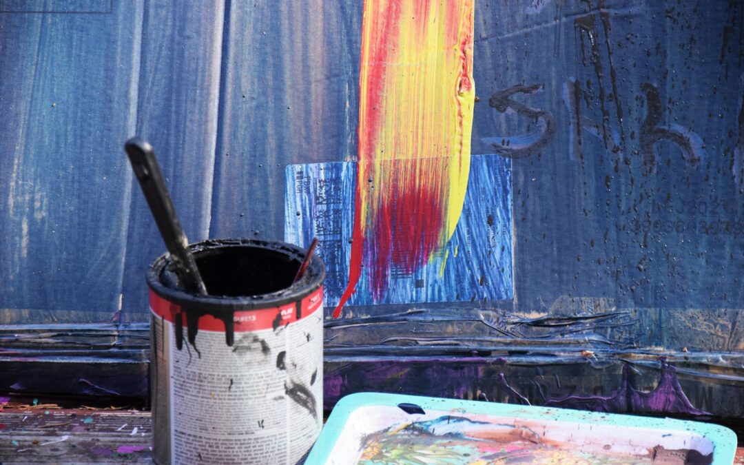 a paint can with a brush in it next to a painting