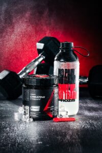Creatine supplement, water bottle, and dumbbells on wet surface